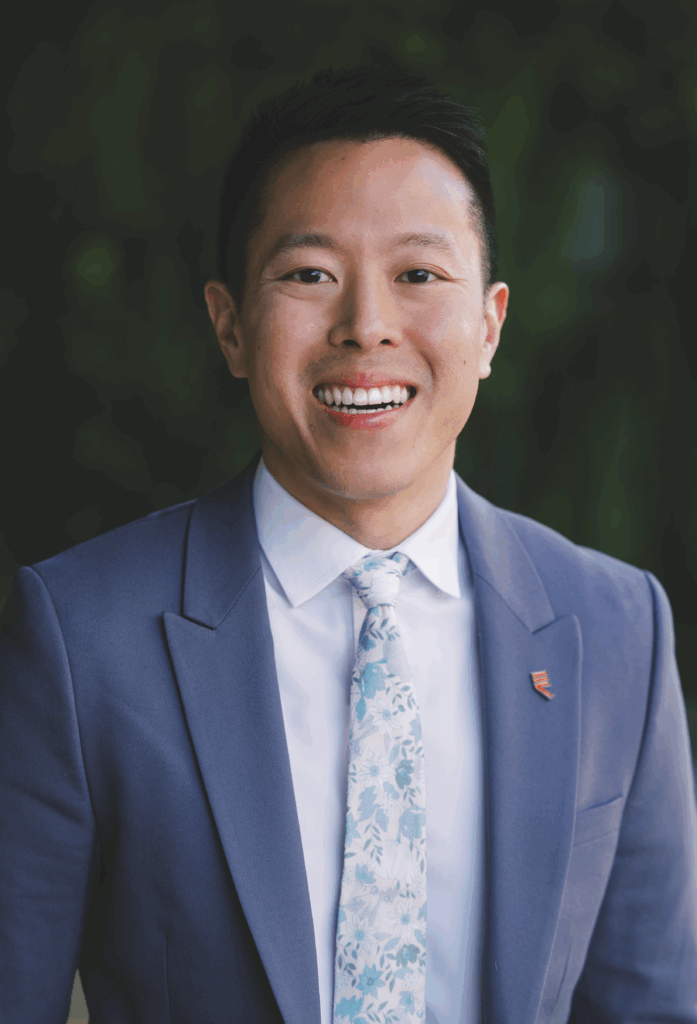 Tony Hoang smiling in a blue blazer, white shirt, and floral tie with an Equality California lapel pin.
