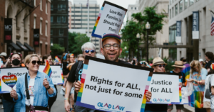 Ricardo Martinez smiling with a sign that reads, "Rights for ALL, not just for some" at the 2026 Boston Pride for the People March.