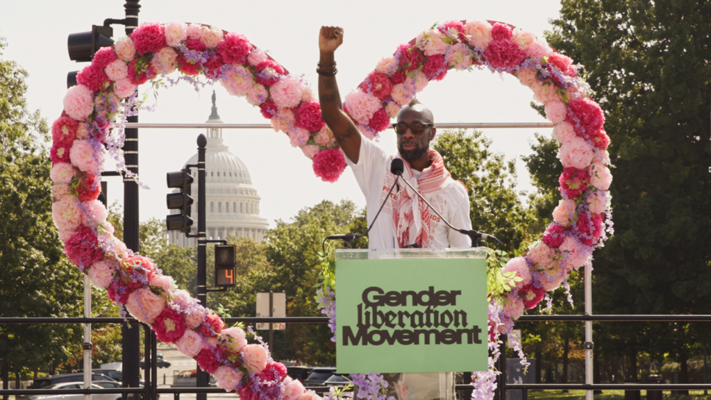 Stephen Chukumba raising his fist at the podium of the Gender Liberation March
