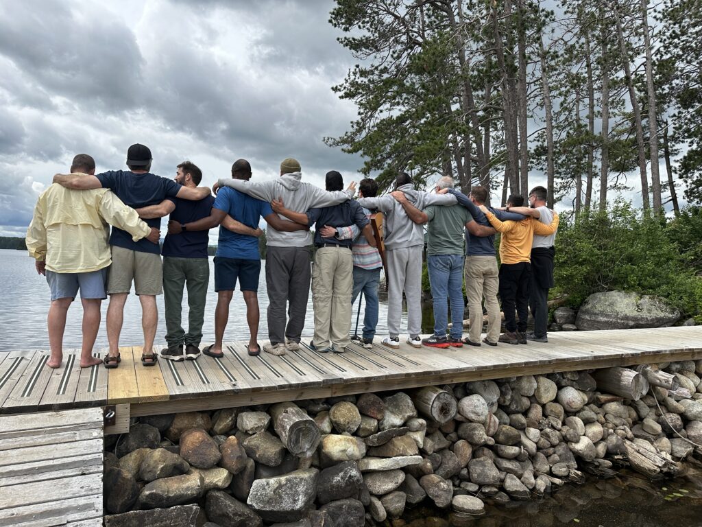 The fathers from The Dads documentary standing arm in arm on a dock looking over water